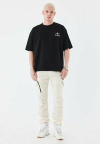 Sort bomulds t-shirt med lille logo på brystet, parret med hvide cargo bukser med lynlåslommer, og hvide sneakers.