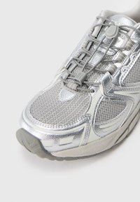 Silver running shoe with mesh upper, reflective accents, and elastic laces. Features a textured sole and padded collar for comfort.