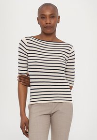 Haut en tricot rayé avec des couleurs bleu marine et crème, à manches courtes et à large encolure bateau. Porté avec un pantalon beige clair ajusté.