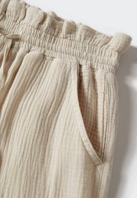 Pantalon en tissu beige froissé avec une taille élastique, des poches latérales et une surface texturée, offrant une coupe décontractée.