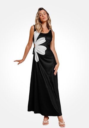 Robe maxi noire avec un grand motif de fleur blanche. Elle présente une découpe sur le côté et un détail à cordon. Tissu lisse, design sans manches.
