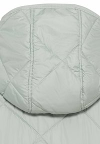 Veste rembourrée légère vert clair avec une capuche. Présente un motif en forme de diamant et des détails piqués, mettant en valeur la texture douce et lisse.
