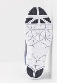 Skoens sål i hvid og blå med et tekstureret grebsmønster, der har et trekantet slidbanedesign og kontrasterende sorte detaljer.
