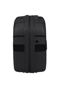 Valise rigide noire avec une texture nervurée, double zip et poignée sur le côté. Dispose d'un petit port pour charger ou pour des accessoires.