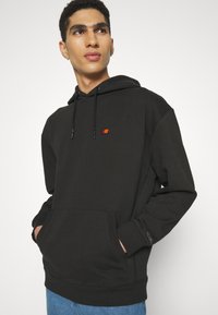 Sudadera negra hecha de una mezcla de algodón, con cordón ajustable, bolsillo tipo canguro y pequeño logotipo multicolor en el pecho.