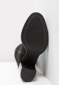 Stivaletto nero con suola in gomma testurizzata, tacco medio a blocco e dettaglio con zip laterale, realizzato in morbida pelle scamosciata.