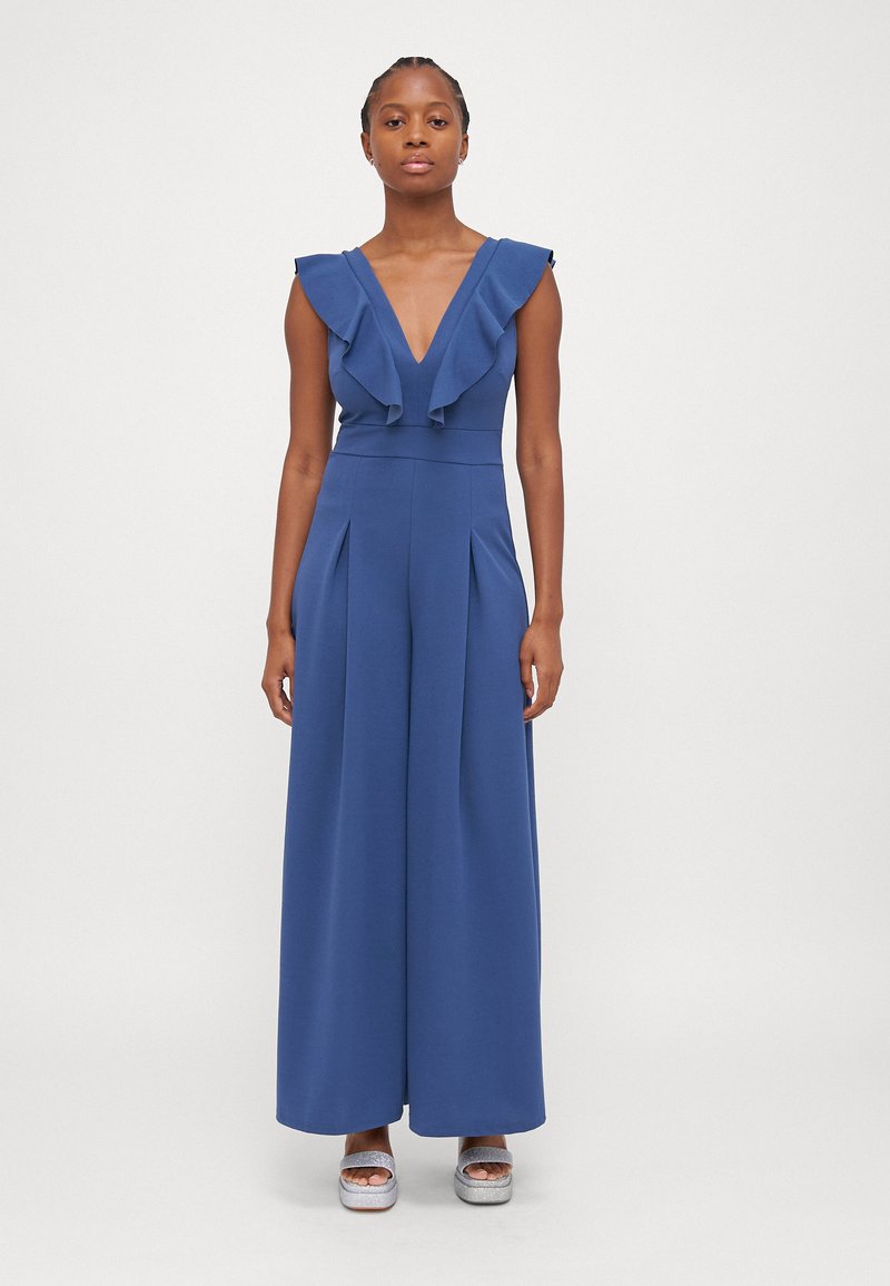 Μπλε φόρεμα ολόσωμου τύπου με ριγέ V-λαιμόκοψη, φαρδιές γάμπες και πλαινά πτυχώσεις. Φτιαγμένο από λείο ύφασμα, έχει εφαρμοστό μέσο και ελάχιστες λεπτομέρειες.