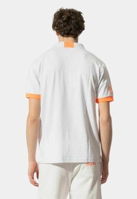 Polo bianco con dettagli arancioni sul colletto e sulle maniche, realizzato in un materiale liscio e leggero, con un dettaglio del logo sulla manica.