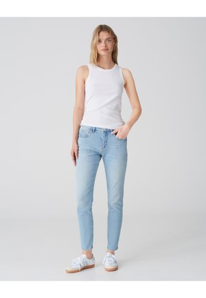 Top a maniche corte bianco con design a costine, abbinato a jeans slim-fit blu chiaro. Il modello indossa sneakers bianche con suola in gomma chiara.