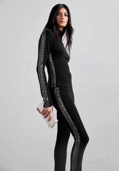 Sort langærmet top og leggings med sølvstuds langs siderne, parret med en hvid studset clutch. Glat stoftekstur.