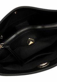 Juodos odos rankinės vidus su užtrauktuku ir auksiniu trikampio formos logotipu bei lygia audinio pamušalu.