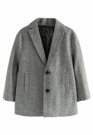 Uldblazer med sort-hvid hundetandsmønster, to forreste knapper, reverskrave og to lodrette slidser i lommerne.