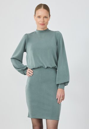 Robe à manches longues et col montant en tissu teal doux et extensible. Présente une silhouette ajustée et un détail de taille froncée. Texture lisse et design minimaliste.