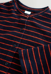 Marineblauwe cardigan met horizontale rode strepen, gemaakt van zachte stof. Voorzien van een ronde halslijn, vier zwarte knopen en geribbelde manchetten.