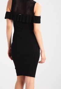 Vestito nero a coste con dettagli a balze scollato sulle spalle e schiena in rete. Il design è aderente, mettendo in risalto la silhouette.