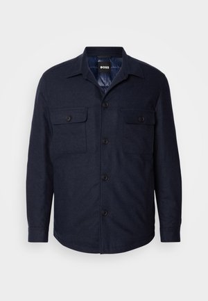 Mørkeblå knap-strikjakke med to brystlommer, en spids krave og en glat tekstur. Har sorte knapper og en afslappet pasform.