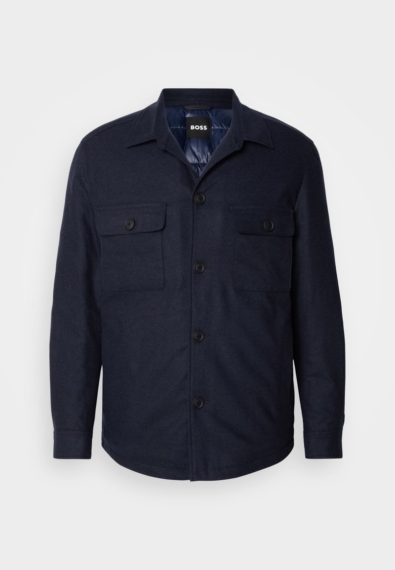 Veste chemise boutonnière bleu marine avec deux poches poitrine, un col pointu et une texture lisse. Présente des boutons noirs et une coupe décontractée.