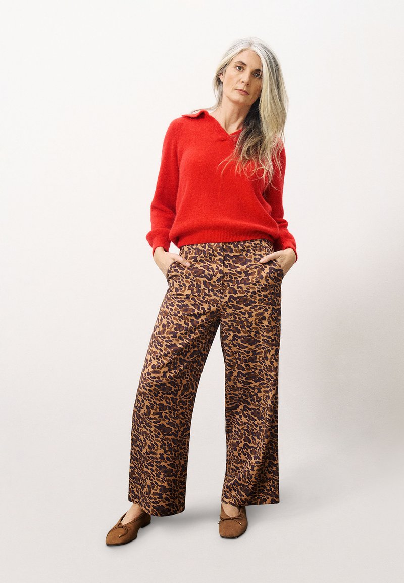 Rode gebreide trui met kraag; brede broek met luipaardprint in bruin en zwart; bruine ballerina's; lang, steil haar.