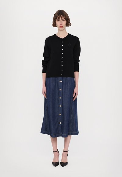 Svart stickad cardigan med knappstängning och subtilt logga; matchad med en blå denimkjol med framknappar och utsvängd nederkant.