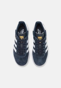 Ναυτικές σουέδ sneakers με τρεις άσπρες ρίγες, μαύρα κορδόνια, επενδεδυμένη γλώσσα και υφή στην εσωτερική σόλα. Χρυσό λογότυπο "adidas" στο πλάι.