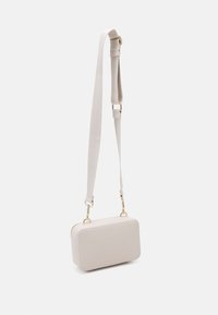Bolso rectangular crossbody en suave material beige con herrajes dorados, correa plana y textura suave. Cuenta con un cierre de cremallera a lo largo del borde.