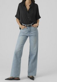 Camicia nera button-up a maniche corte, abbinata a jeans a gamba larga di un blu chiaro. Accessoriata con una cintura nera e ballerine nere a punta.