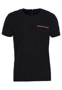 Schwarzes Baumwoll-T-Shirt mit kurzen Ärmeln, ausgestattet mit einer kleinen Brusttasche, die mit roten, weißen und blauen Streifen akzentuiert ist. Klassischer runder Ausschnitt.