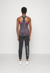 Svart och rosa mönstrad linne med racerbackdesign, kombinerat med svarta joggingbyxor med vit grafisk text. Vita sneakers.