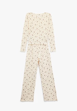 Conjunto de pijama color crema con mangas largas y pantalones, presenta un patrón marrón repetido de pequeños lazos. Tejido suave, corte relajado.