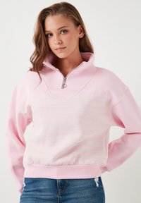 Felpa leggera di colore rosa chiaro con colletto a zip quarti, caratterizzata da strisce orizzontali verde pastello e polsini e orlo a costine.