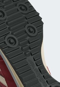 Adidas apavu zole, kas veidota no teksturētas melnas gumijas ar apaļām un lineārām rakstām, ko norobežo krēmkrāsas vidussole.