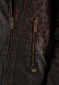 Braune und schwarze Lederjacke mit Leopardenmuster und messingfarbenen Reißverschlüssen, Nahaufnahme des Brustbereichs mit zwei vertikalen Reißverschlüssen.