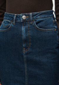 Gonna in denim blu scuro con bottoni frontali e tasche, indossata con un top nero.