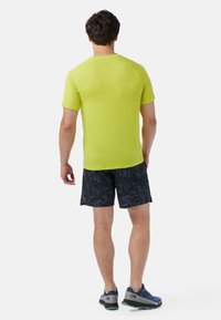 Kortærmet, lys limegrøn træningsskjorte parret med mørke, mønstrede shorts. Har raglanærmer og en afslappet pasform.