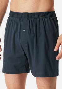 Boxers en coton bleu marine avec une taille élastique, fermeture à bouton à l'avant, et texture lisse. Pas de motifs ou d'accents visibles.