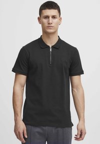 Černé polo tričko vyrobené z bavlněné směsi, s límcem na zip a krátkými rukávy. Obsahuje decentní logo na hrudi.