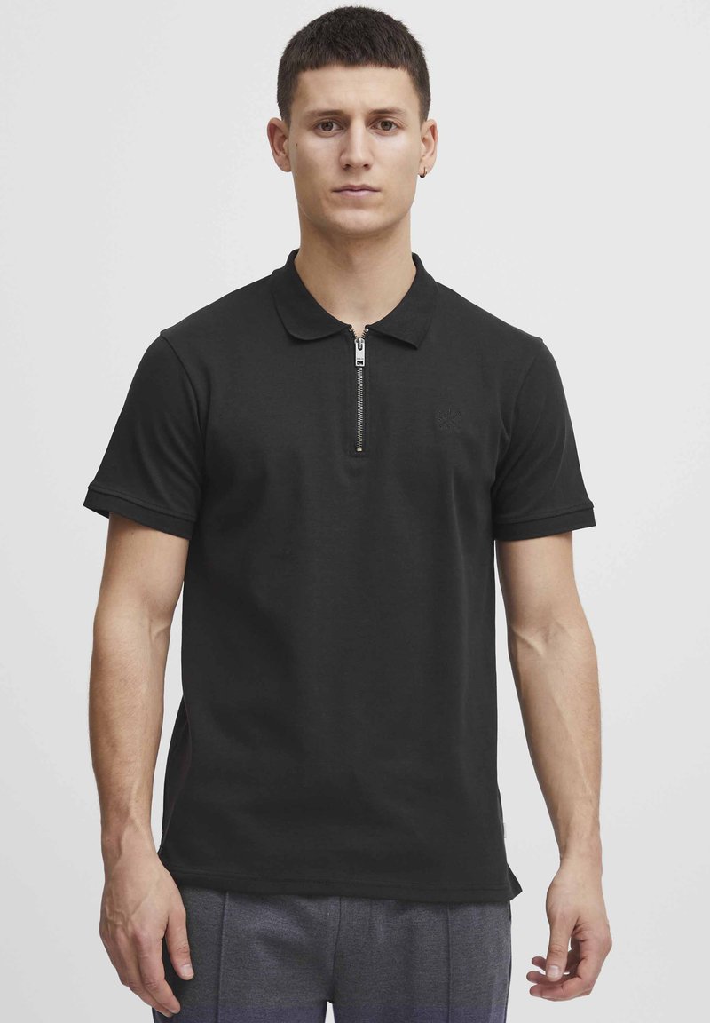 Černé polo tričko vyrobené z bavlněné směsi, s límcem na zip a krátkými rukávy. Obsahuje decentní logo na hrudi.