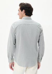 Lichtgrijze lange mouwen shirt met een button-down kraag, rugvork en verstelbare manchetten. Gladde textuur met een subtiele afwerking.