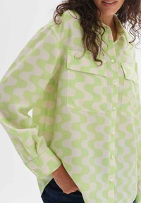 Light green button-up shirt with a wave pattern in white, featuring two chest pockets, long sleeves, and a relaxed fit.