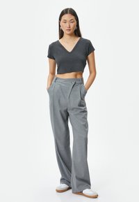 Grå cropped t-shirt med V-hals, parret med højhalsede grå brede bukser med sidelomme og knapdetalje. Hvide sneakers.