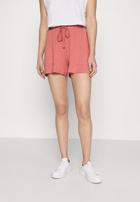 Pantaloni shorts rosa in cotone con vita regolabile, due tasche frontali e una vestibilità comoda, abbinati a sneakers bianche.