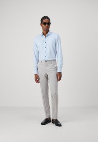 Cămașă albastru deschis cu nasturi negri, asortată cu pantaloni slim-fit gri deschis și mocasini negri. Modelul poartă ochelari de soare negri.