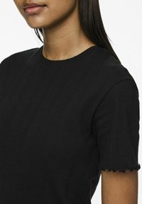 Svart strikket topp med et teksturert design med ribbete mønstre og bølgete korte ermer. Rund hals. Myk stofffinish.