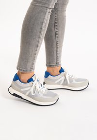 Graue und weiße Sneakers mit blauen Akzenten, aus Mesh und Wildleder. Sie verfügen über eine abgerundete Zehenpartie, eine dicke Sohle und weiße Schnürsenkel.