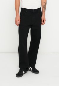 Blugi negri cu croi larg, din denim rezistent, având un design tradițional cu cinci buzunare și cusături subtile. Împerecheați cu adidași negri și o cămașă albă.