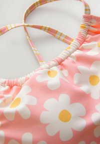 Top di bikini rosa con motivi a margherita bianchi e centri gialli. Presenta spalline sottili a righe e una texture arricciata lungo i bordi.