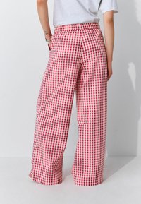 Red and white gingham check wide-leg pants with an elastic waistband, smooth texture, and loose fit. Detailed with side pockets.