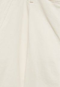 Gros plan sur un tissu beige avec des coutures visibles et une couture diagonale, montrant la texture et les plis du matériau du vêtement.