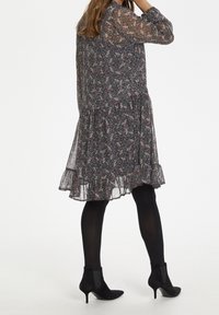 Blumenkleid in dunklen Tönen mit Schichten-Saum, transparenten langen Ärmeln und Rüschendetails. Kombiniert mit schwarzen Ankle-Boots und Strumpfhosen.