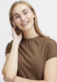 Brun kortærmet top med plisseret halsudskæring, der har en glat tekstur og slim fit, velegnet til casual eller semi-formelt tøj.